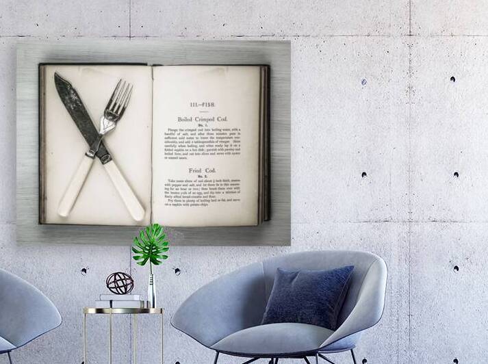 Old cookery book open with an old fork spoon and table knife by Assaf Frank