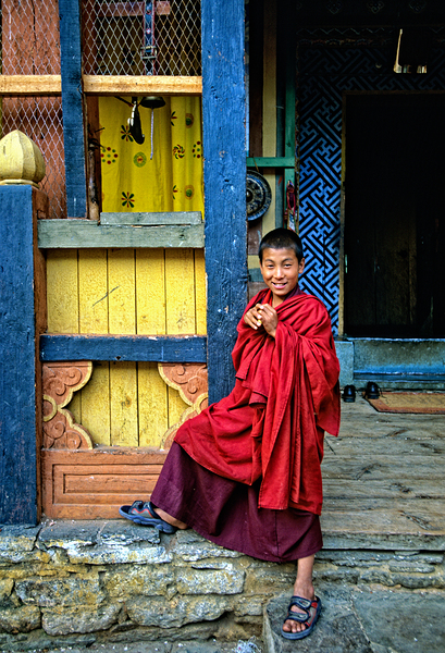 Smiling young monk in red robes at colorful traditional building Digital Download