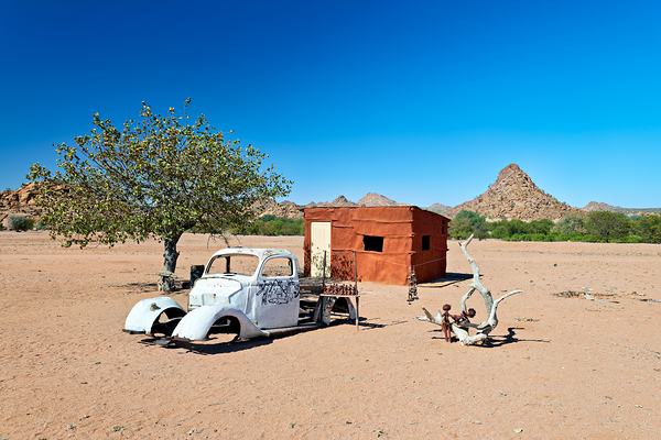 Classic car wreck in Namibias desert landscape near a structure Digital Download