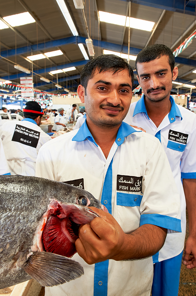 Smiling fishmongers hold fresh fish at market in Dubai UAE Digital Download