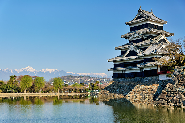 Matsumoto Castle stands beside water with mountains in the dista Digital Download