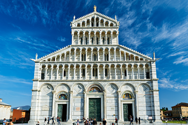 Visitors walk around Pisa Cathedral in Piazza dei Miracoli. The tall structure stands under a blue sky. People enjoy the lively atmosphere. Digital Download