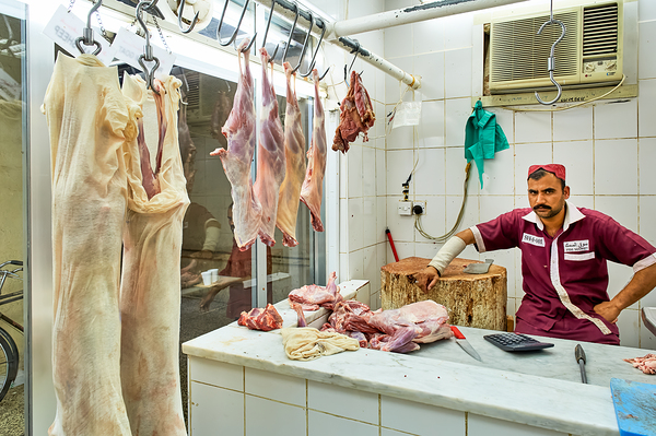 Butcher works in meat market in Dubai with hanging meat Digital Download