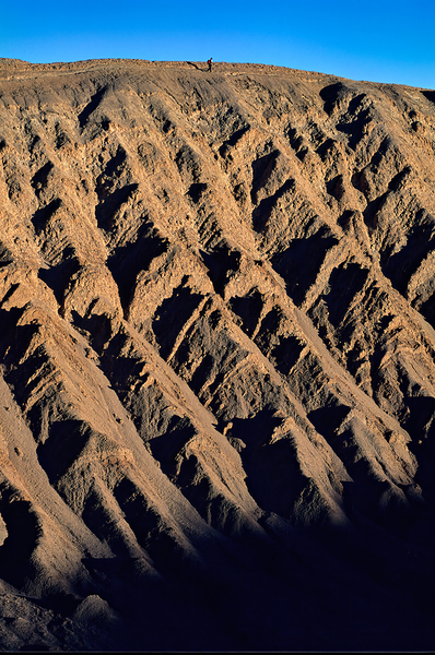 Hiker traverses a dramatic shadowed desert landscape. Digital Download