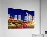 People walk across the Helix Bridge as the Marina Bay Sands Hotel shines at sunset. The sky turns orange and lights reflect in the water. Acrylic Print