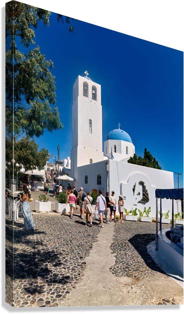 Greek village street with white church blue dome and tourists.