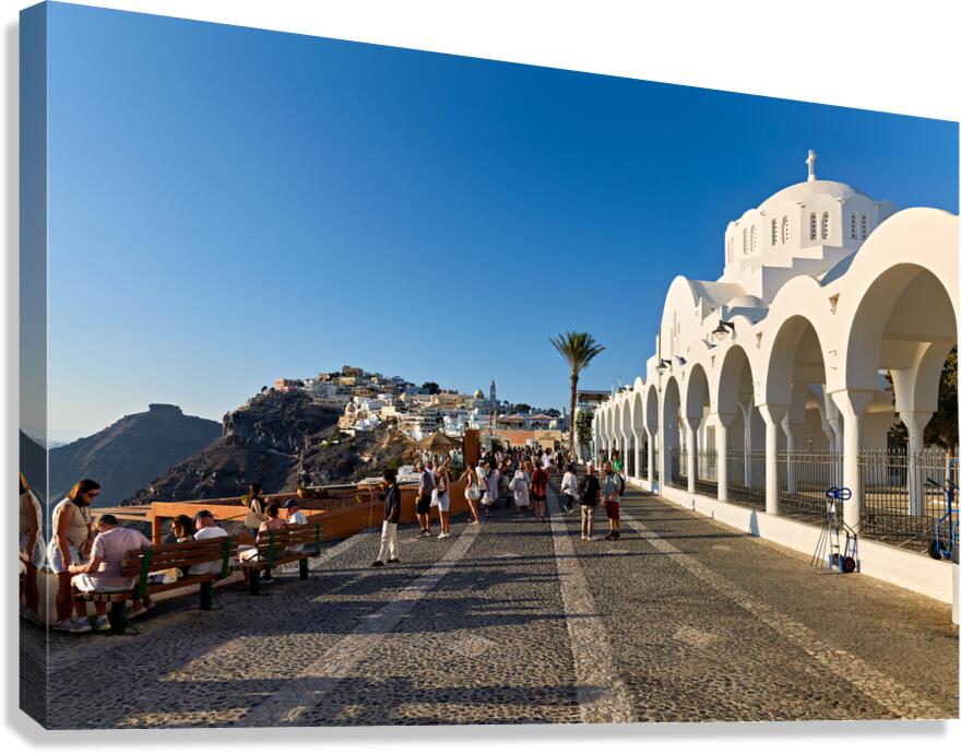 Crowds walk past white church cliffside town in Santorini.