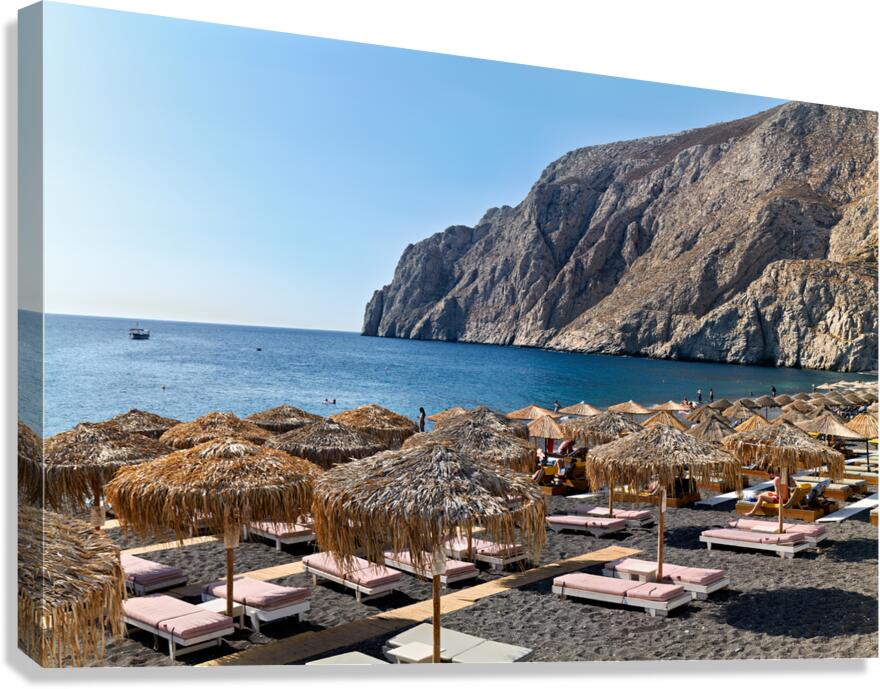 Scenic black sand beach with straw umbrellas and rocky cliffs.