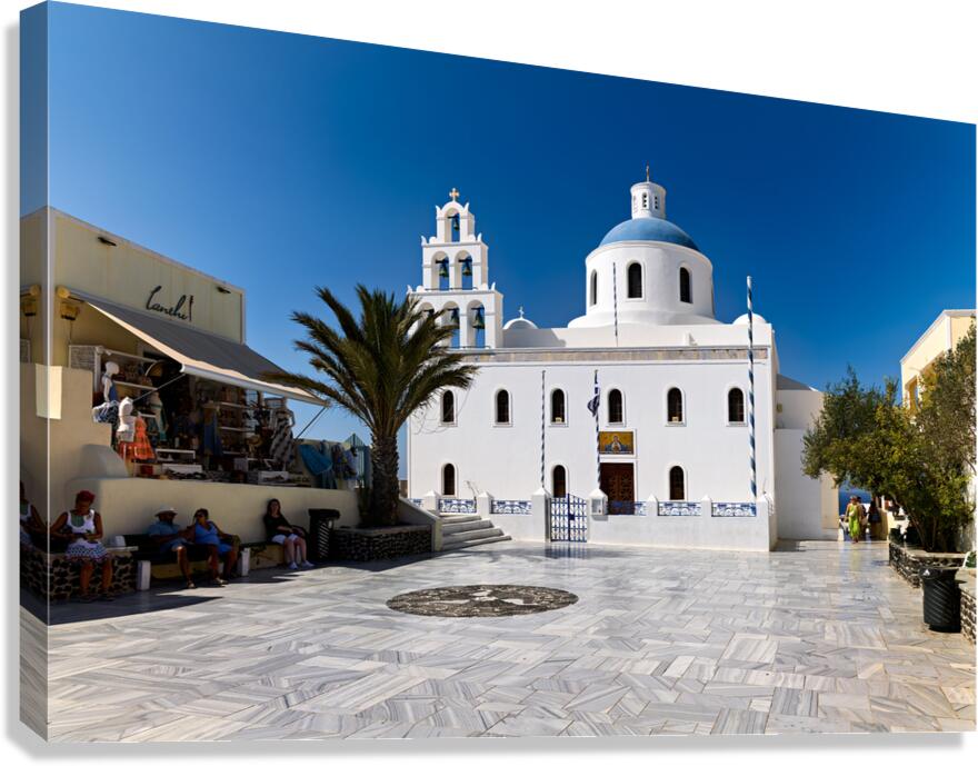 White Greek church with blue dome in sunny town square.