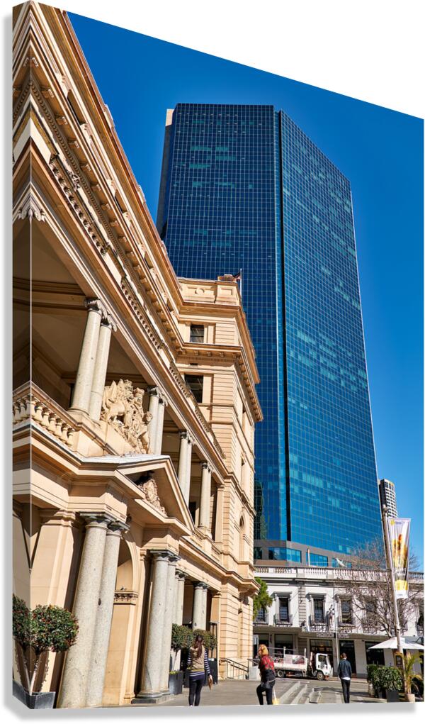 Modern skyscraper dwarfs historic building under clear blue sky.