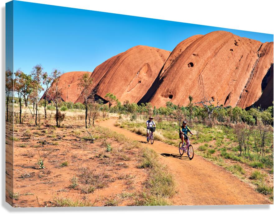 Two cyclists ride on a dirt path near Uluru Australia.