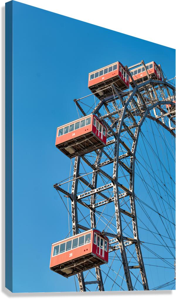 Ferris wheels red cabins against a clear blue sky.