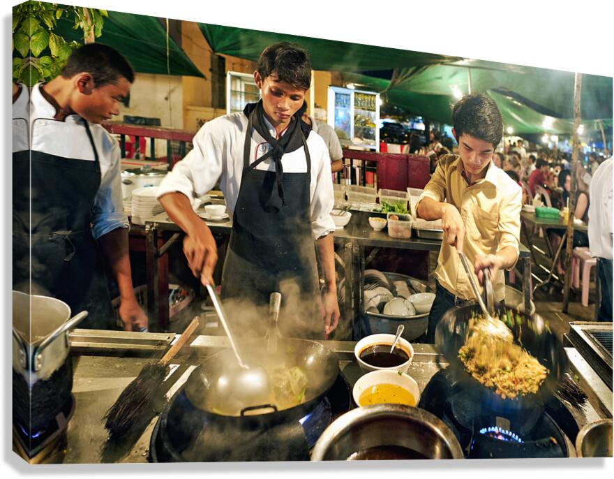 Three chefs cook steaming street food in woks at night.