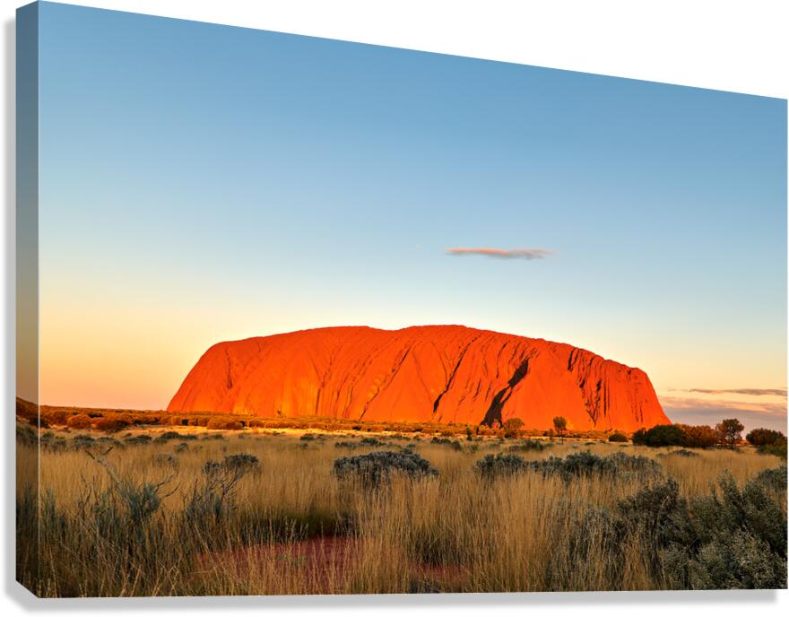 Uluru glows orange at sunset with a vast grassy plain.