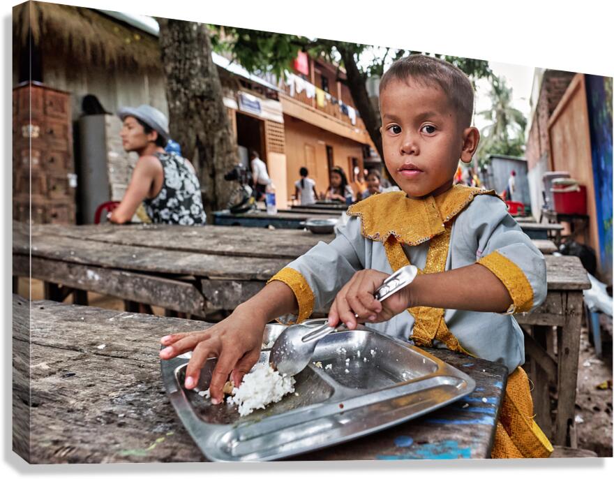 Child in traditional dress eating rice outdoors.