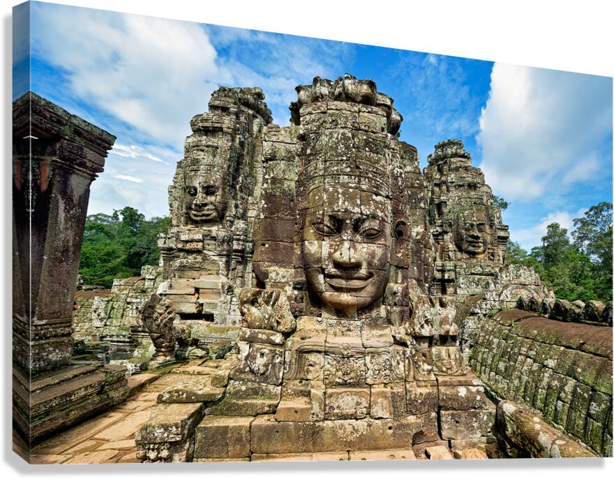 Ancient stone faces on Bayon Temple under a blue sky.