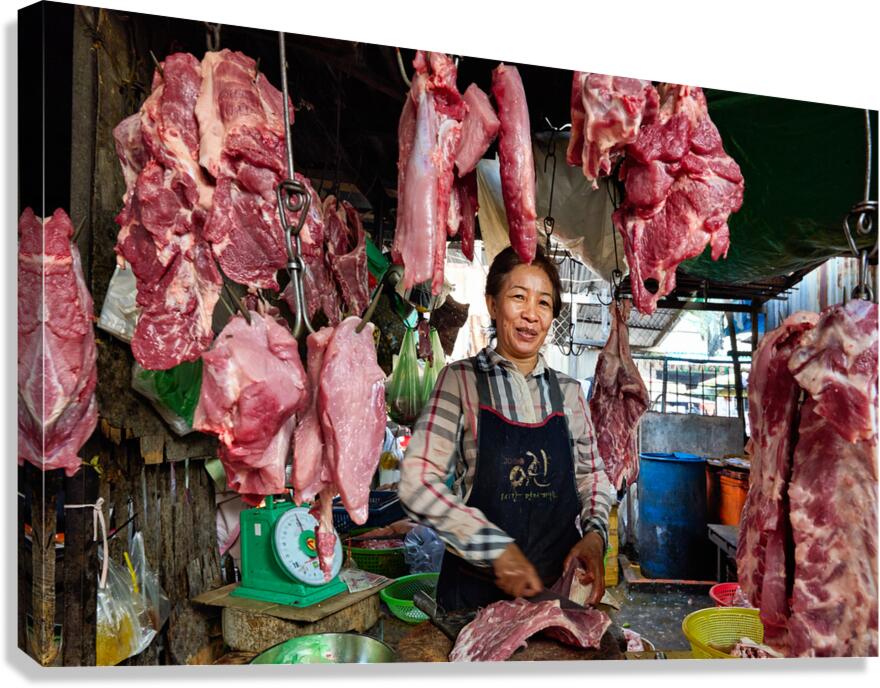 Woman butcher at market stall with hanging raw meat.