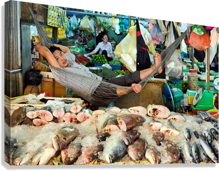 Market vendor relaxes in hammock above fresh fish.