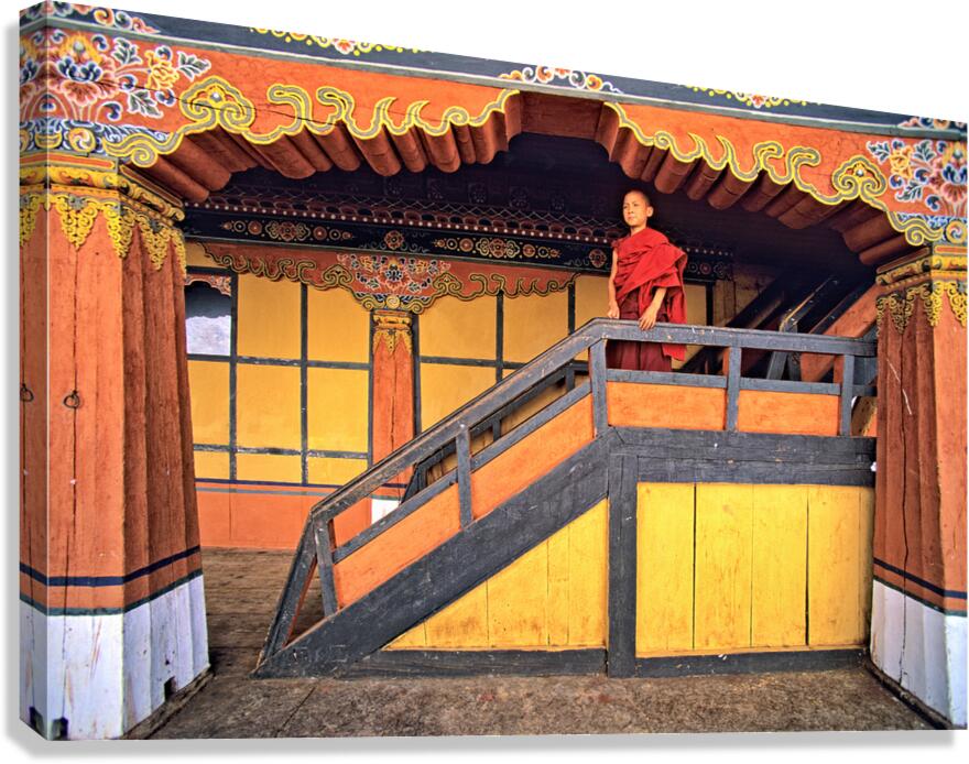 Young monk in red robes on colorful temple staircase.