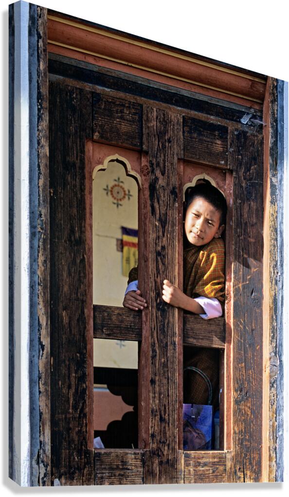 Bhutanese child peeking from ornate wooden window.