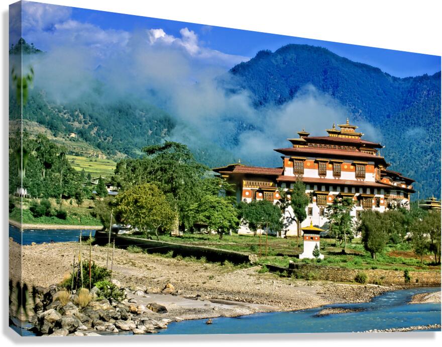 Bhutanese monastery by river with misty mountains.