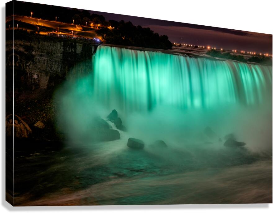 Niagara Falls illuminated green at night with spectators.