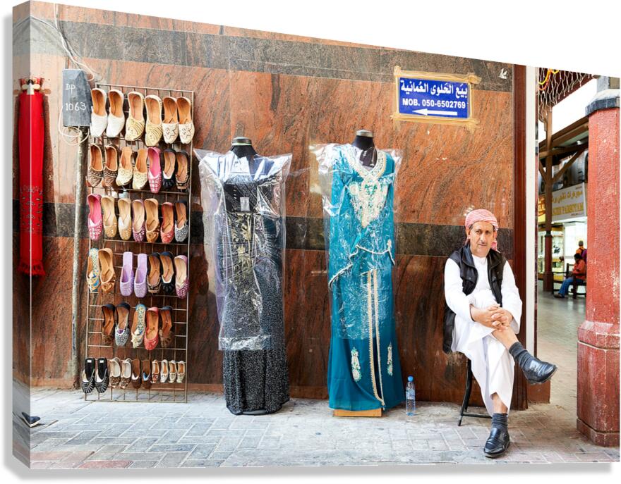 Man sits by shoes and dresses while relaxing in Dubai market