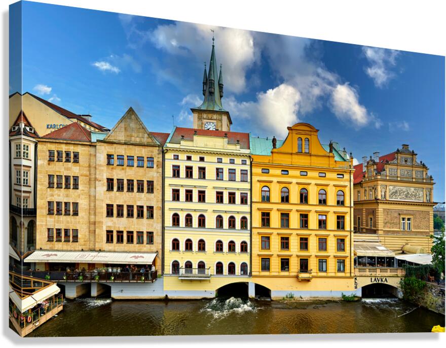 Historic Prague buildings and clock tower line a scenic river.