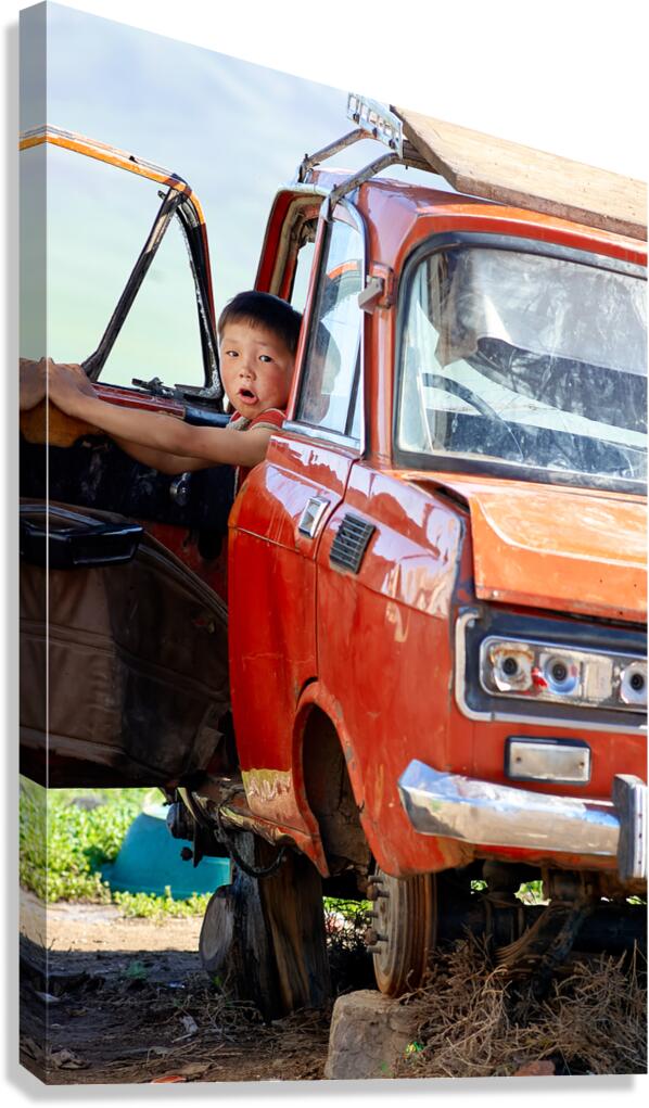 Boy sits in a wrecked car in Mongolia
