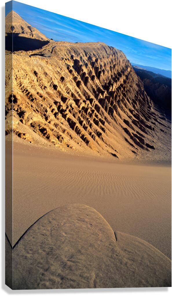 Eroded desert mountains and rippled sand under blue sky.