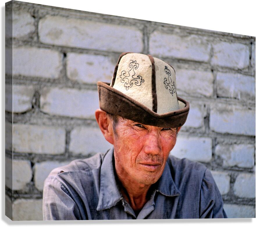 Man in traditional hat sits against a brick wall in Bukhara