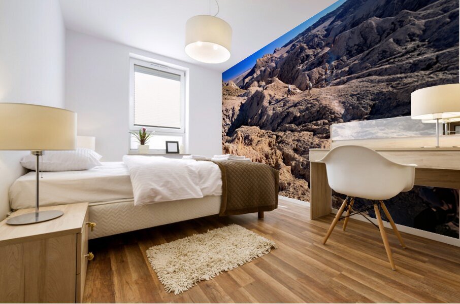Hikers traverse a vast arid rocky desert landscape. Mural print