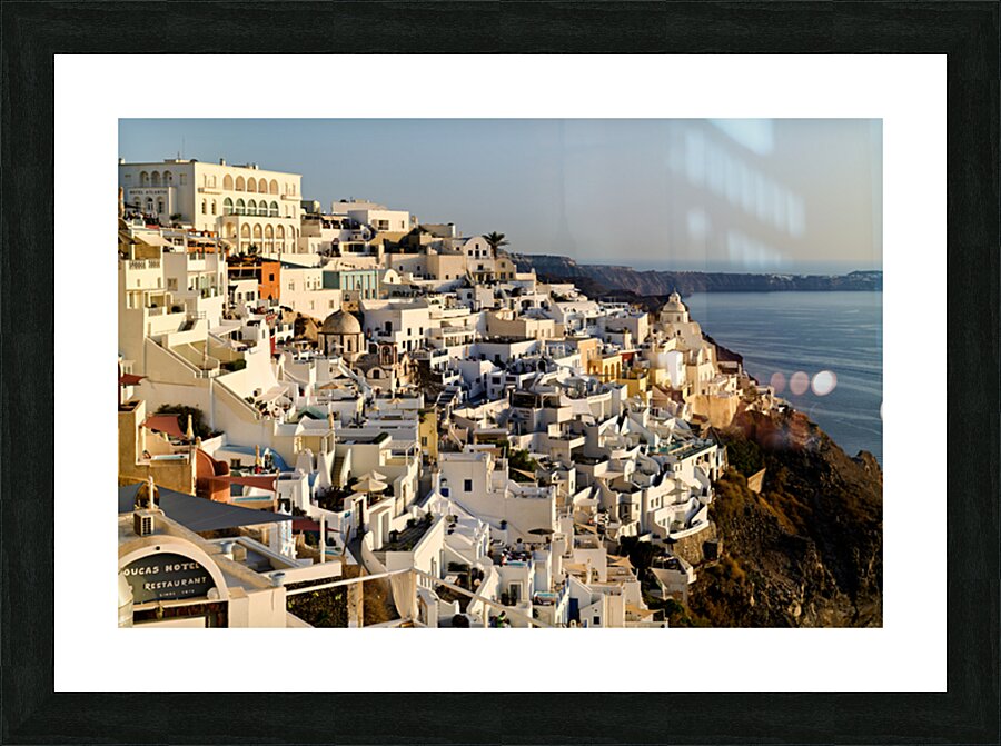 Santorinis white buildings cascade down cliff to the sea. Picture Frame print