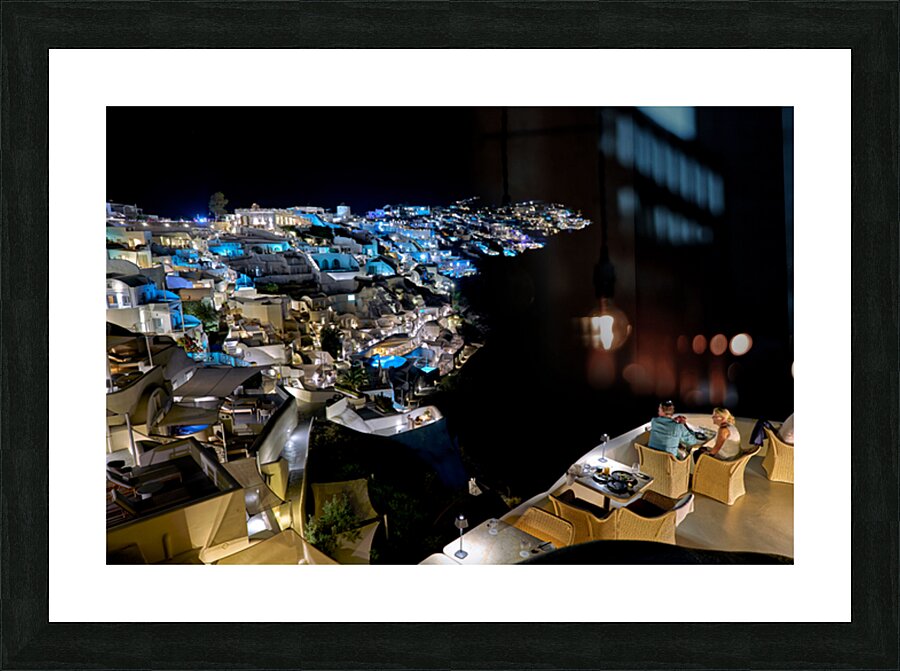 Illuminated cliffside town at night couple enjoying dinner. Picture Frame print