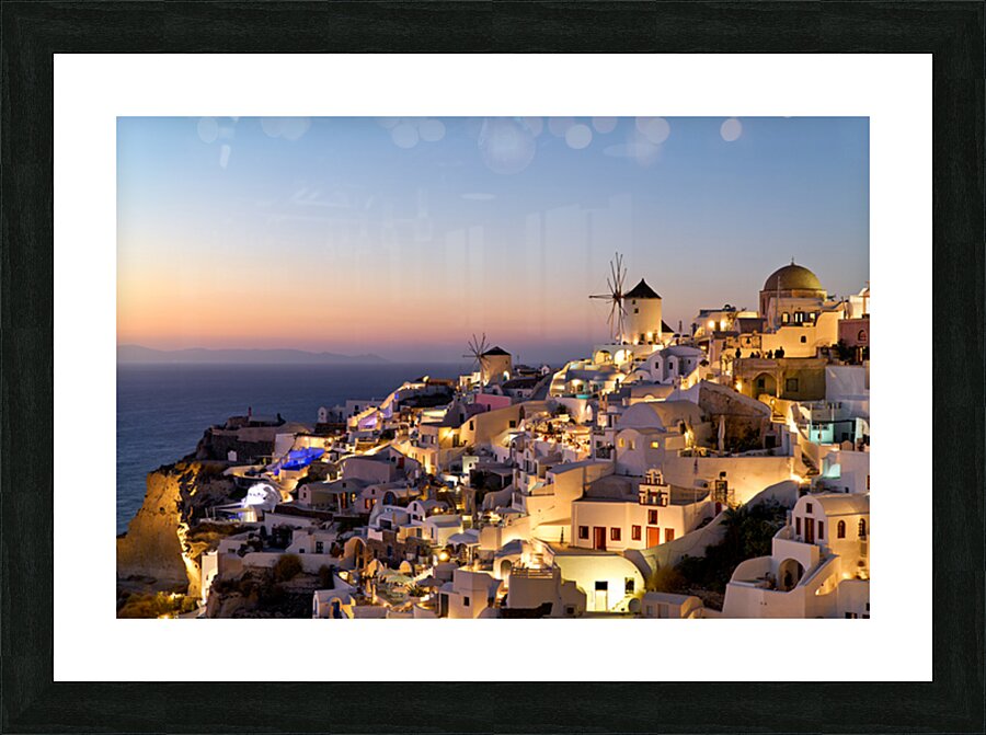 Santorinis Oia village glows at twilight by the sea. Picture Frame print