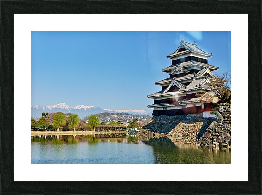 Matsumoto Castle stands beside water with mountains in the dista Picture Frame print