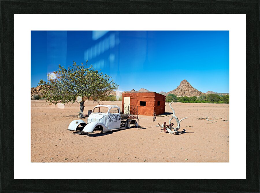 Classic car wreck in Namibias desert landscape near a structure Picture Frame print