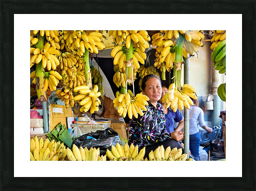 Market vendor surrounded by abundant yellow bananas. Picture Frame print
