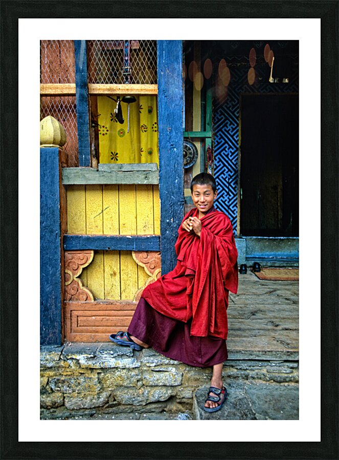 Smiling young monk in red robes at colorful traditional building Picture Frame print