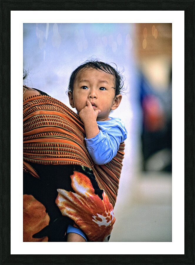 Curious child carried in a patterned fabric sling. Picture Frame print