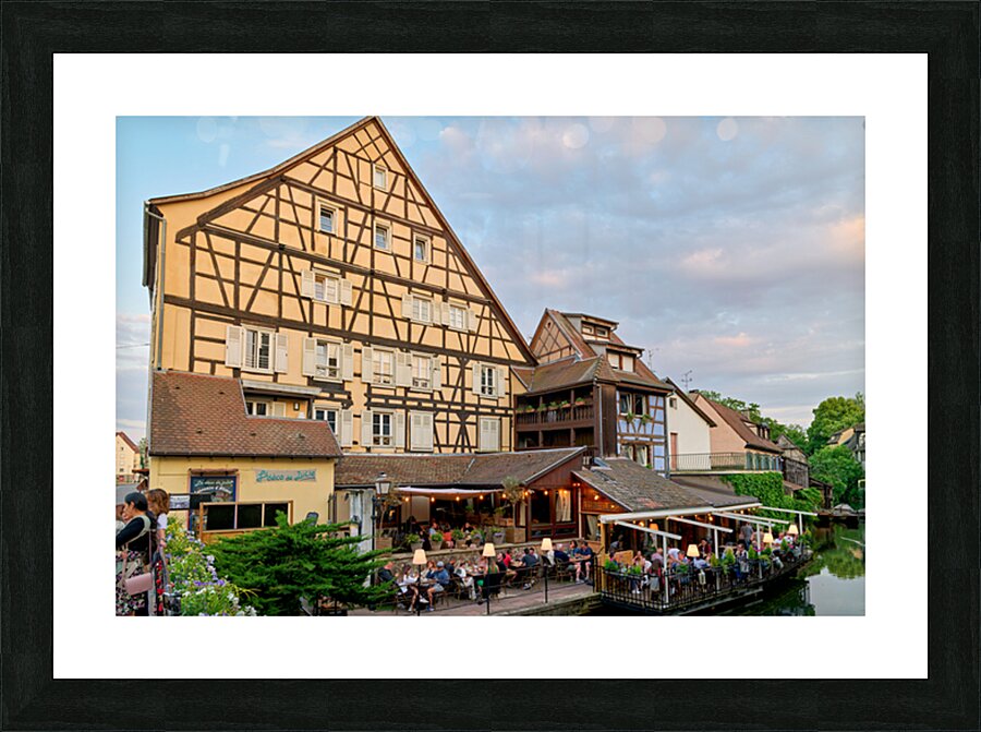 Dining by the canal in Colmar with timber framed houses in view Picture Frame print