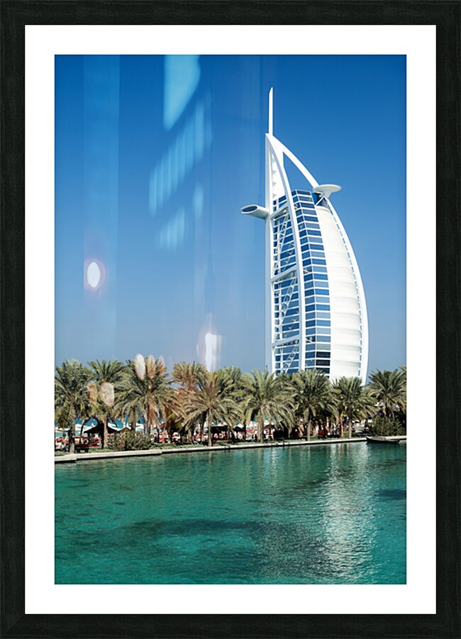 Burj Al Arab hotel stands tall by the water with palm trees Picture Frame print