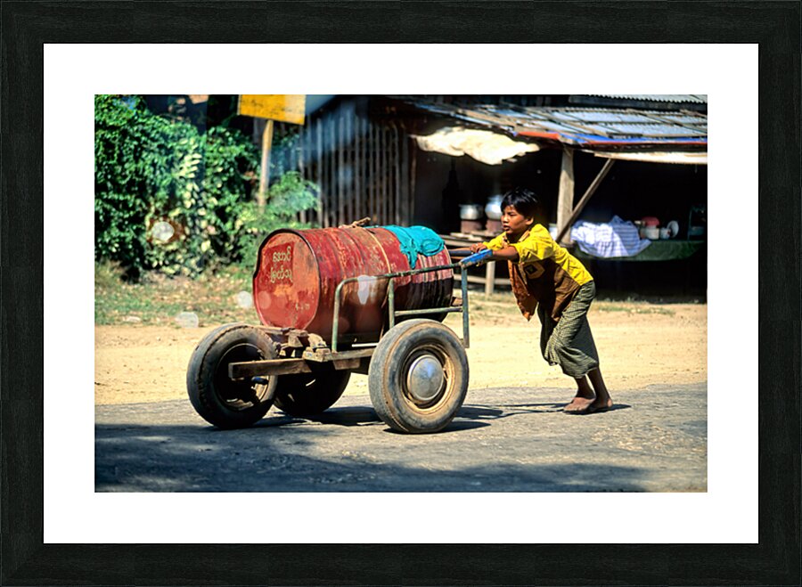 Boy pushes a cart down the street in Myanmar during the day Picture Frame print