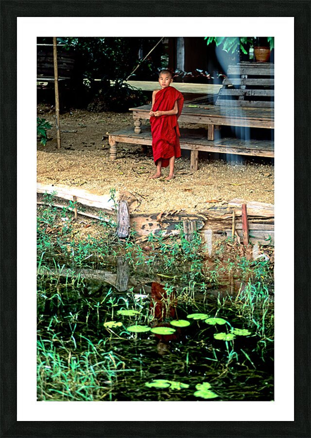 Young monk stands by water in Myanmar during daytime Picture Frame print