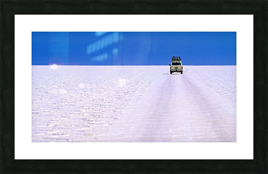 Van driving across vast white salt flat under blue sky. Picture Frame print