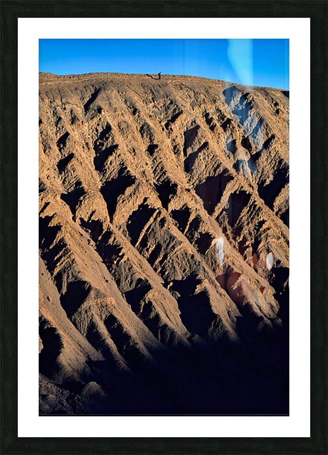 Hiker traverses a dramatic shadowed desert landscape. Picture Frame print
