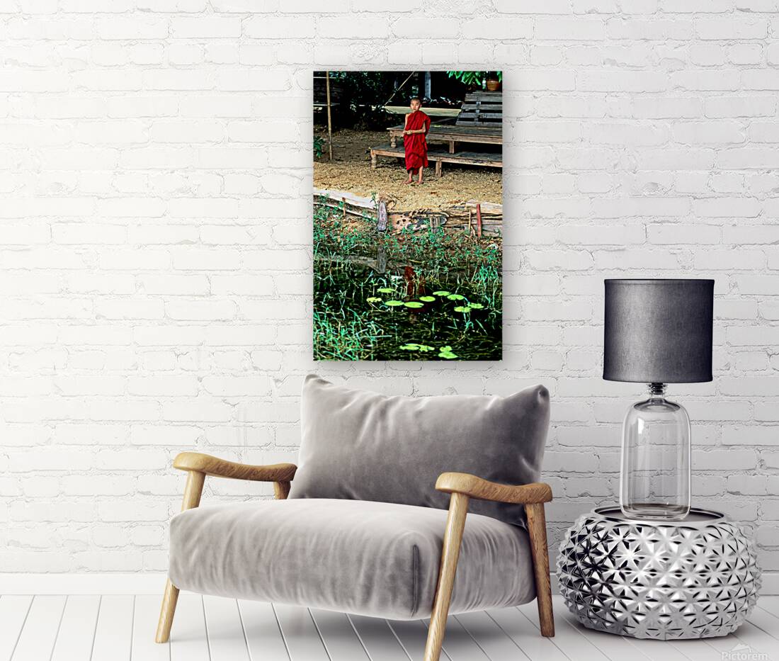 Young monk stands by water in Myanmar during daytime Reproduction