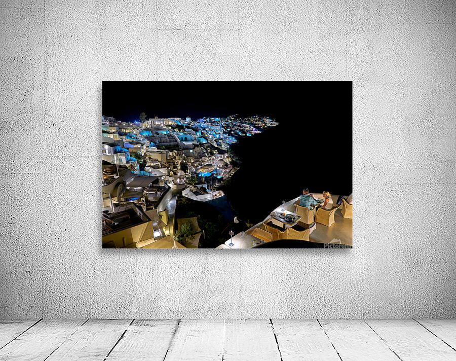 Illuminated cliffside town at night couple enjoying dinner. Wall Preview