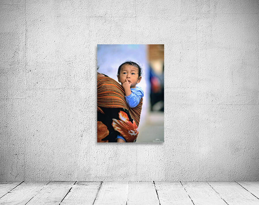 Curious child carried in a patterned fabric sling. Wall Preview