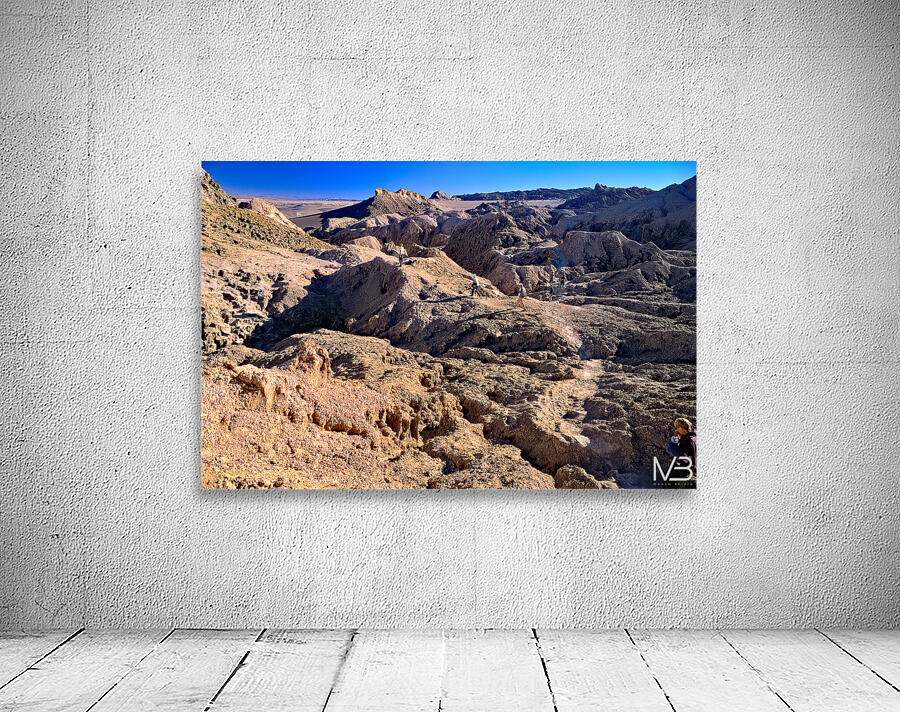 Hikers traverse a vast arid rocky desert landscape. Wall Preview